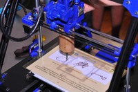 Detall d'una impressora 3D reproduint unes signatures amb xocolata